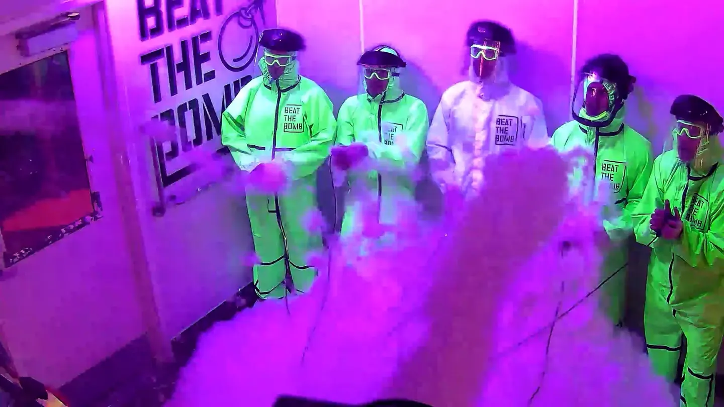 Players in black hazmat suits posing by the neon Bombie mascot wall