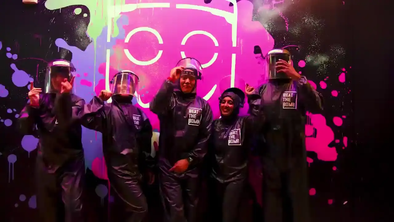 Players in black hazmat suits posing by the neon Bombie mascot wall